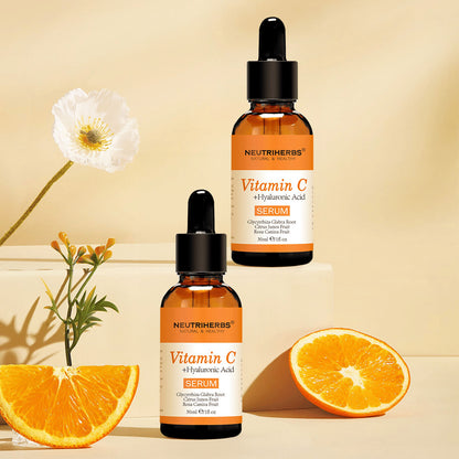 Neutriherbs Vitamin C + Hyaluronic Acid Serum 30 ml skupaj s svežimi pomarančami in cvetovi. Navdihujoča produktna fotografija, ki poudarja vsebnost vitamina C v serumu za navlaženo kožo, večji sijaj in bolj enakomeren ten kože.